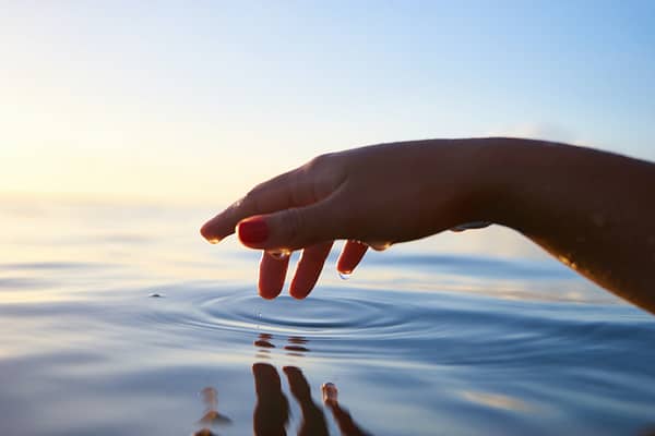 A hand poised over water, fingers making peaceful little ripples