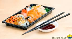 A black plastic tray laden with a delectable array of sushi, sashimi, ginger and wasabe, and alongside it chopsticks and a dish of soy sauce.