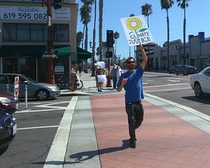 Man in blue shirt holding sign showing a large yellow flower and the words "Climate Justice," at Oceanside CA Climate Strike demonatration Sept. 20, 2019