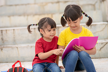 Little Asian girl and her sister reading story books
