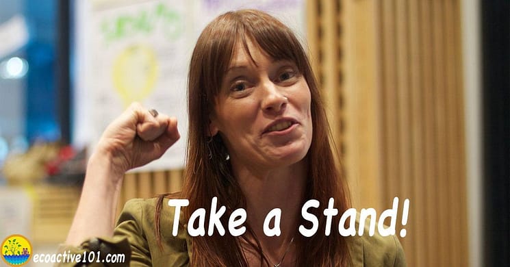 A young woman stands up in a meeting with raised fist, taking a stand for nuclear safety. The text says, “Take a stand!”